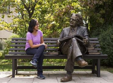Apala Das poses for a photo with a statue of Northrop Frye at Victoria College in the University of Toronto