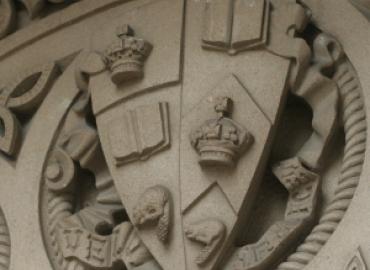 U of T coat of arms in stone on a building.