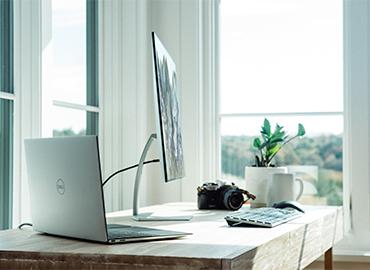 Table with a desktop computer, laptop, camera, plant and mug