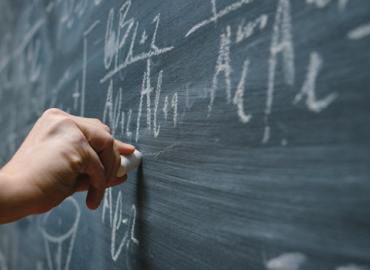 A hand writing math equations with white chalk on a blackboard. 