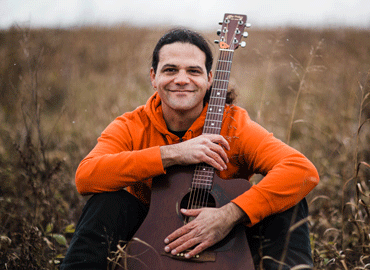 Joe Reilly sitting in a field with guitar