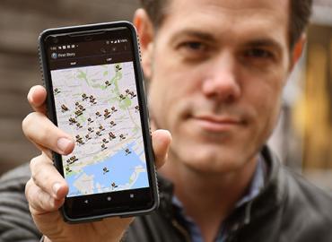 Jon Johnson holds a smartphone with his First Story Toronto app on the screen