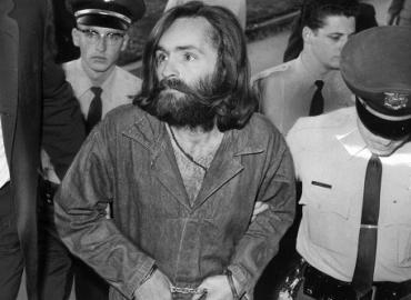 Charles Manson in handcuffs walking with a police officer