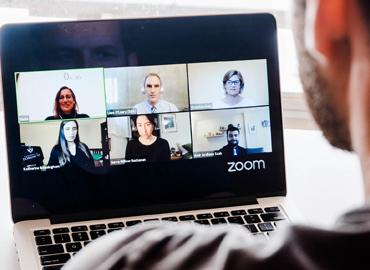 Over the shoulder view of a laptop screen with six presenters on Zoom. Over the shoulder view of a laptop screen with six presenters on Zoom.