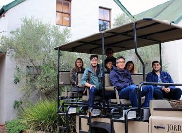 Kim Stead with Professor Joseph Wong and students sitting in an open vehicle outside a small building in South Africa.