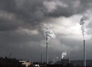 Smokestacks billow into a dark, grey sky.