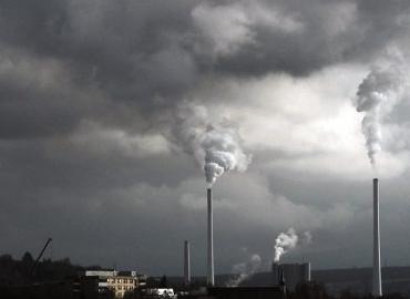 Smokestacks billow into a dark, grey sky.