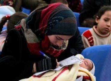 A refugee filling an application while holding her baby at the UNHCR registration center in Tripoli, Lebanon.
