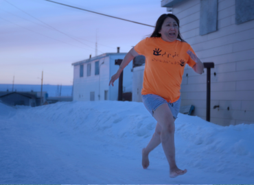 Woman running barefoot in shorts and t-shirt on snowy road