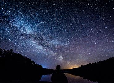 Person standing gazing out at mountain and stars at night