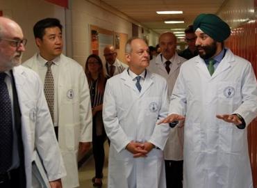 Scott Mabury and Meric Gertler with federal innovation minister Navdeep Bains in lab coats walking down a hallway.