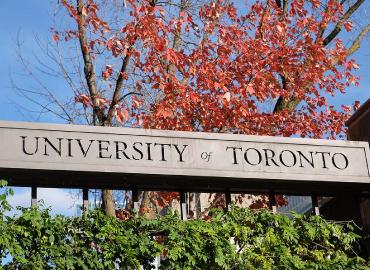 A stone banner over top of the gates of College st. that says University of Toronto.