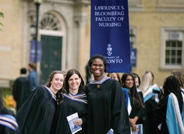 A group of people in convocation robes post for the picture. The Faculty of Nursing blue banner is in the background.