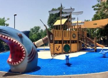 A playful pirate-themed playground with a ship, shark, and teeter totter dolphins.