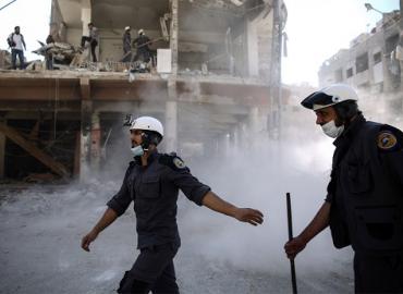 First responders in Douma, Syria wear helmets and masks as they walk amidst rubble