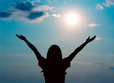 woman with arms raised facing sun
