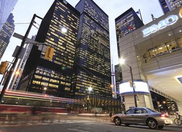 A busy street in Toronto&amp;#039;s financial district, with a car and streetcar in the foreground and skyscrapers in the background.