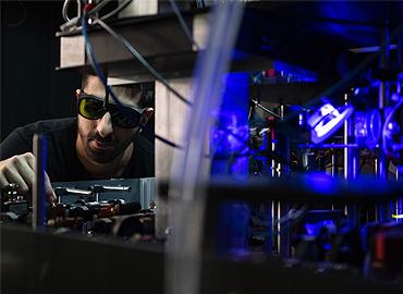 A man peering into a technical device that is glowing blue from within