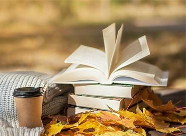 a stack of books lies near a warm scarf and hot coffee against the background of yellow leaves.