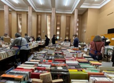Shoppers browse through many books that line long tables in a large room.