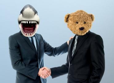 Two businessmen shaking hands one with a superimposed shark head and the other with a teddy bear head.