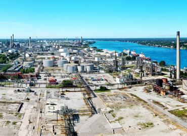An aerial panorama of chemical plants by a river under a bright blue sky.