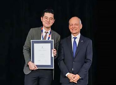 Jonathan Chen and U of T president Meric Gertler standing on a stage holding a certificate in a frame.