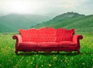 Red sofa in a grassy field with hills behind it