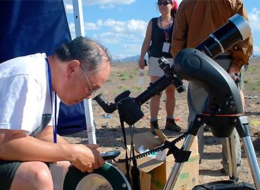 Ralph Chou looking through a telescope in the middle of a field on a sunny day.