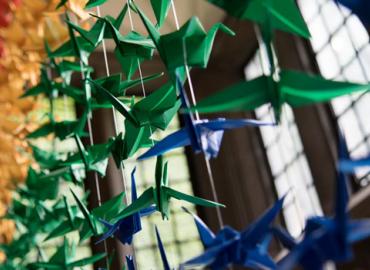 A close-up image of rainbow paper cranes hanging in a large window at Hart House.