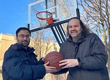 Two men holding a basketball in front of a net