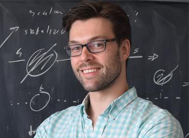 Headshot of David Curtin in front of a blackboard covered in equasions