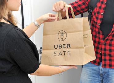 A person handing another person dinner in an Urber Eats paper bag.