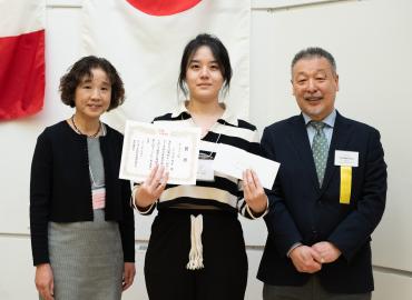 A femalr student holding a certificate flanked by a woman and a man in business wear