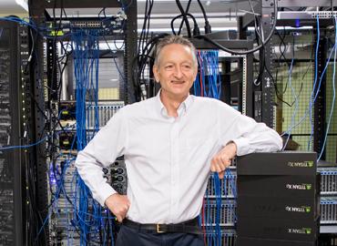 Geoffrey Hinton standing in front of a massive bank of computer hardware