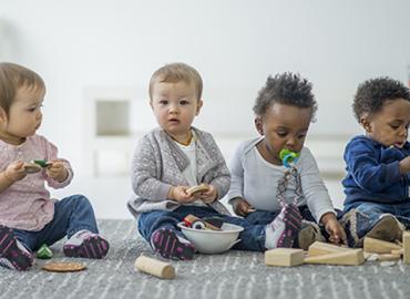 A group of four babies sitting on the floor, playing with blocks. 