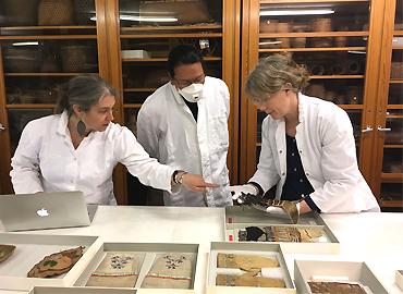 Three researchers looking at artifacts on a table.