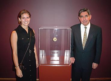 Bonnie Hiltz with former President of Costa Rica Óscar Arias Sánchez stand beside a glass case with a Nobel Peace Prize medal inside. 