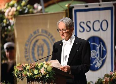 Geoffrey Hinton delivers a speech on a stage during the Nobel Prize.