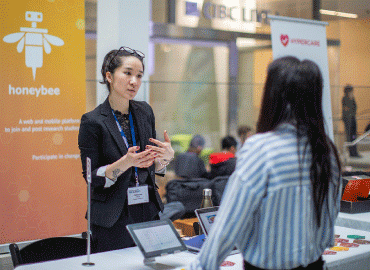 One person speaking to another in front of a large yellow banner at entrepreneurship week.