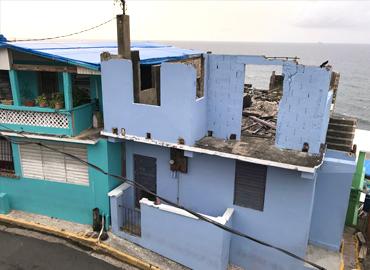 A purple house by the sea with a damaged roof