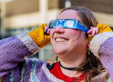 Ilana MacDonald demonstrates the safe way to watch the eclipse - as she holds safety glasses to her eyes.