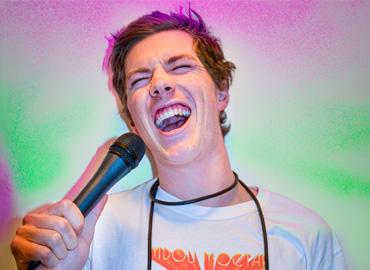 A young man holding a microphone; mouth open; expression of joy