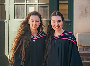 two women standing side by side in graduation gowns
