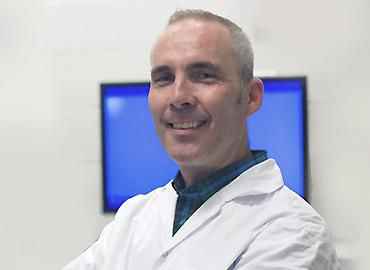 John Peever in a white coat in front of a TV screen