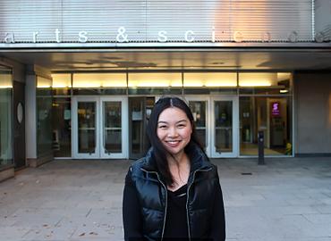 Jolie Gan standing in front of doors with the words Arts &amp;amp; Science on them