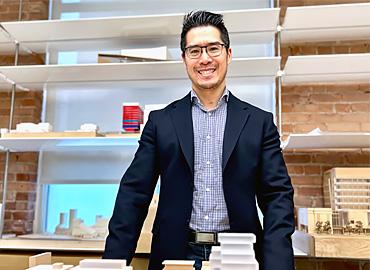 Joseph Yau standing behind table with architectural models on it and also behind him on shelves