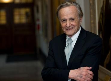 John Polanyi standing and smiling with arms crossed in a dark suit and mint green tie