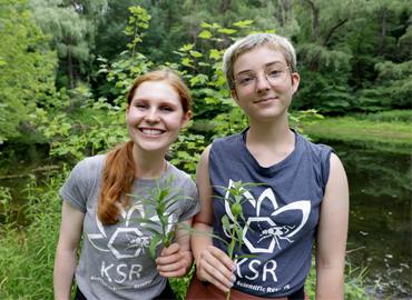 Abigail Wagner (l.) and Lily Peters (r.) at the Koffler Scientific Reserve standing in front trees holding branches in their hands