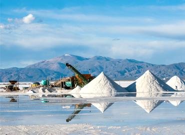 A lithium mine at Salinas Grandes in the salt desert of Jujuy province, Argentina.  Three huge piles of salt and machinery are visible on the flat plain